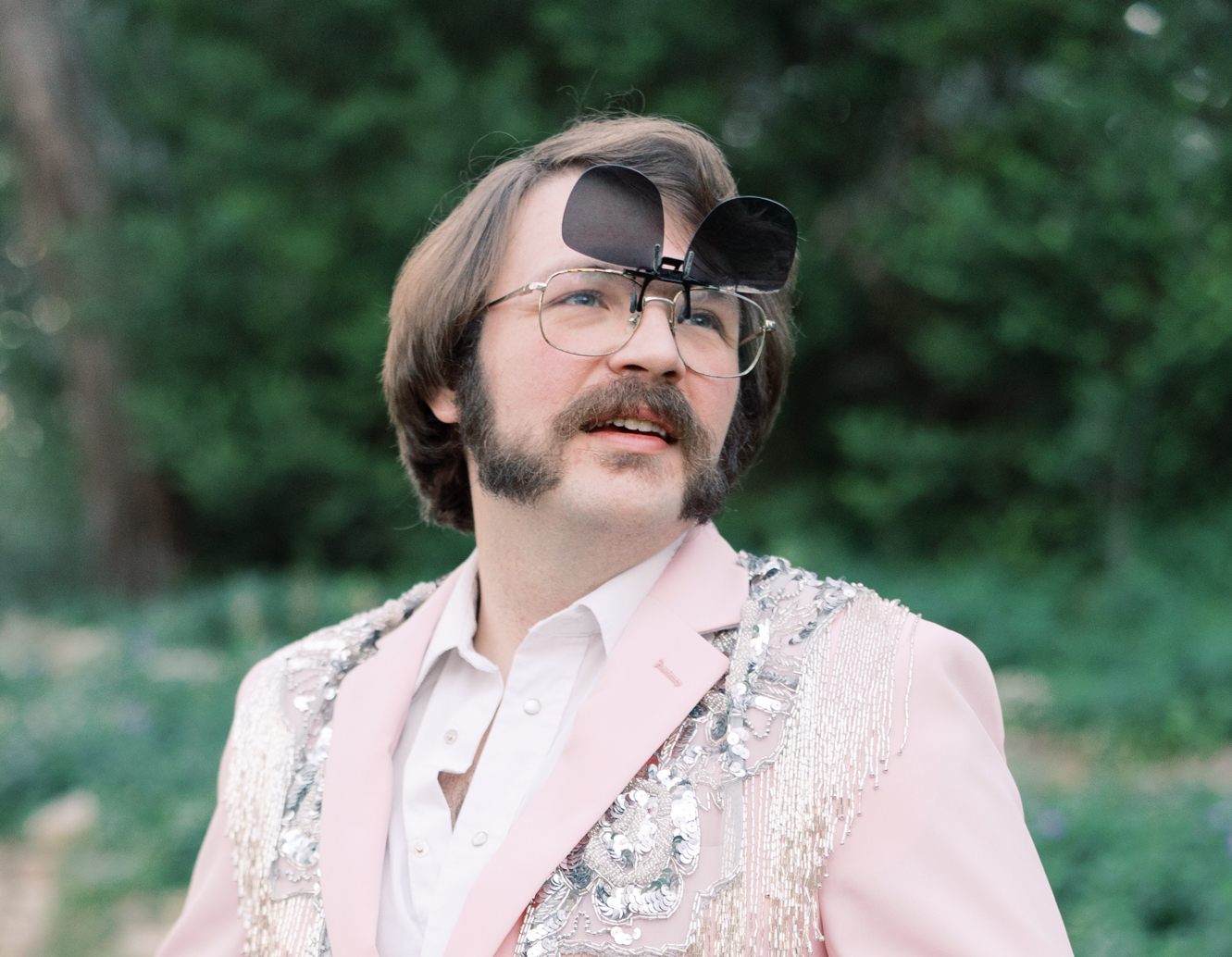 our author: a young-ish man in a pink rhinestone suitcoat wearing aviator eyeglasses with sunglass flip-ups donning a jovial smile